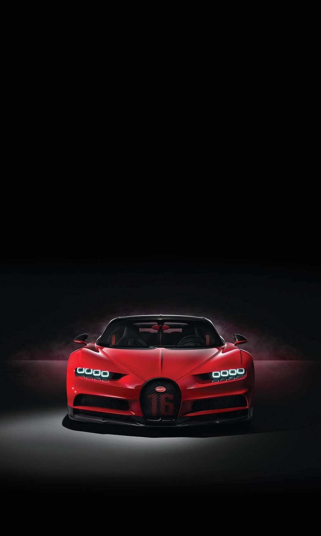 Red Bugatti Chiron supercar featuring a 16 badge on the grille and glowing LED headlights in a dark studio.