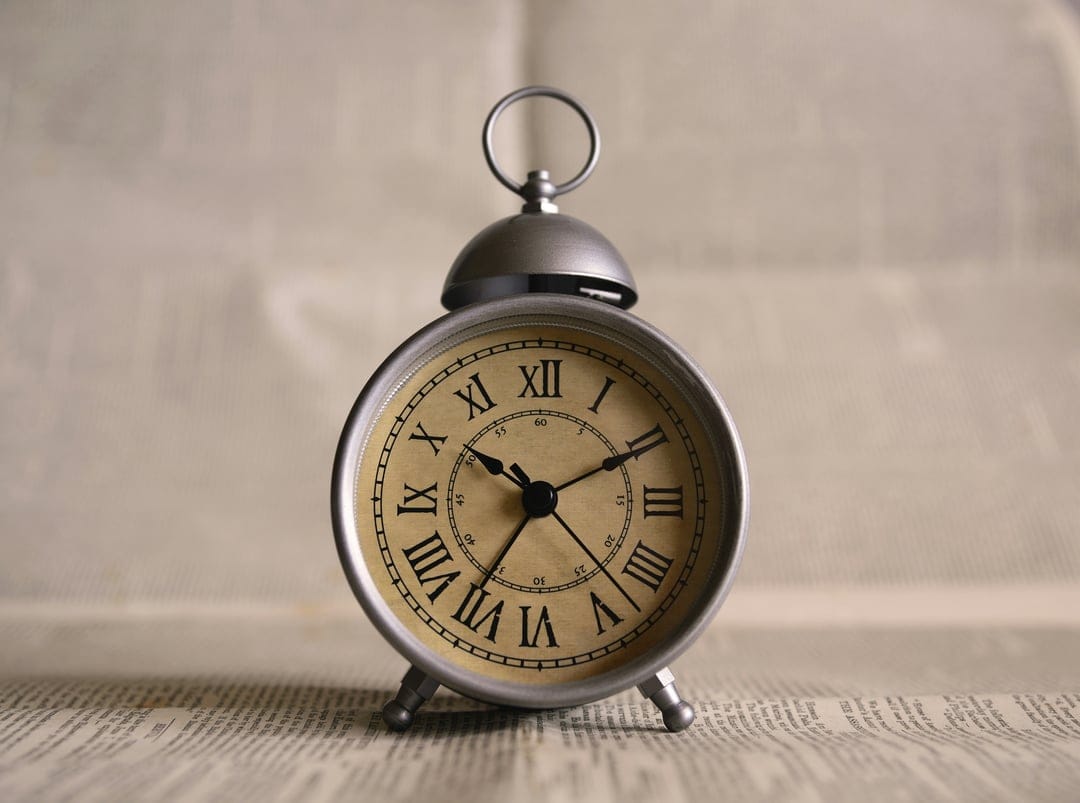 Vintage silver alarm clock with Roman numerals on newsprint under soft light for a vertical screen display.