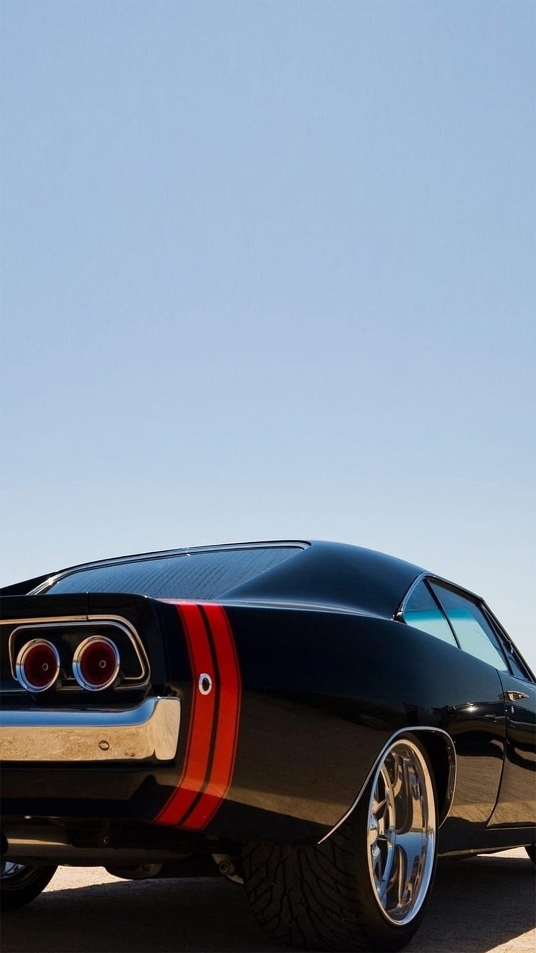 Black Dodge Charger rear view showing dual red taillights, chrome bumper, and racing stripes against a blue sky.