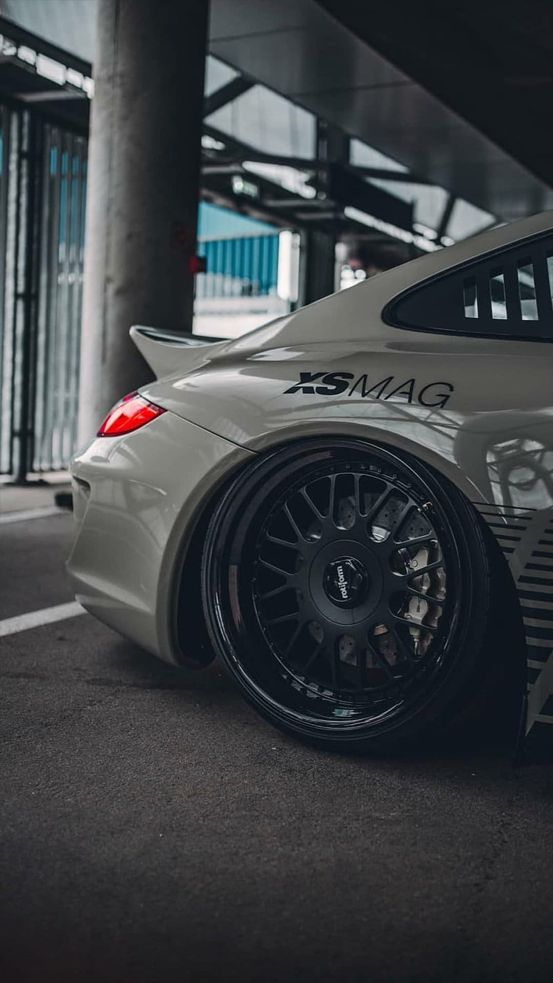 White Porsche rear quarter panel showing custom black multi-spoke wheels, a red taillight, and XSMAG decal.