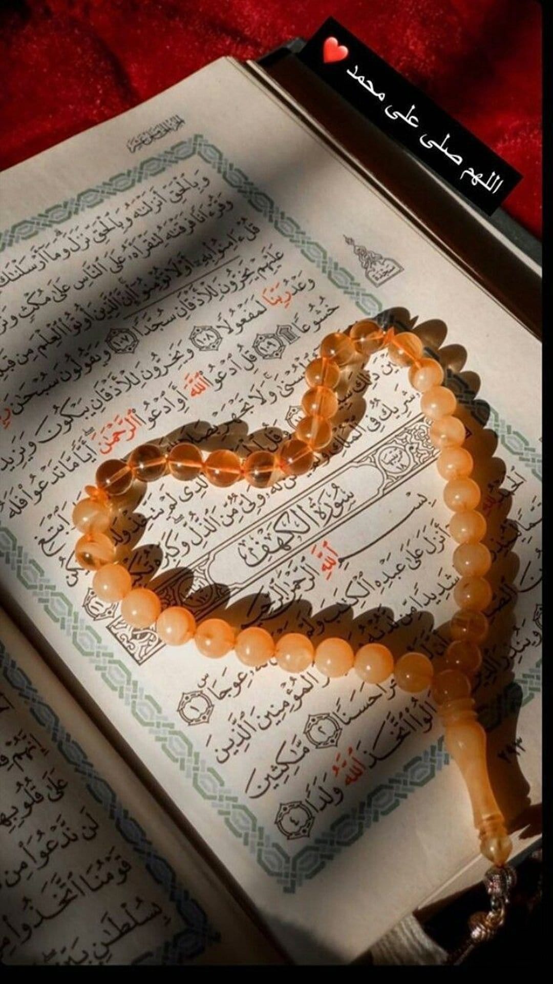 Amber prayer beads draped over an open Quran with Arabic script illuminated by warm, glowing natural light.