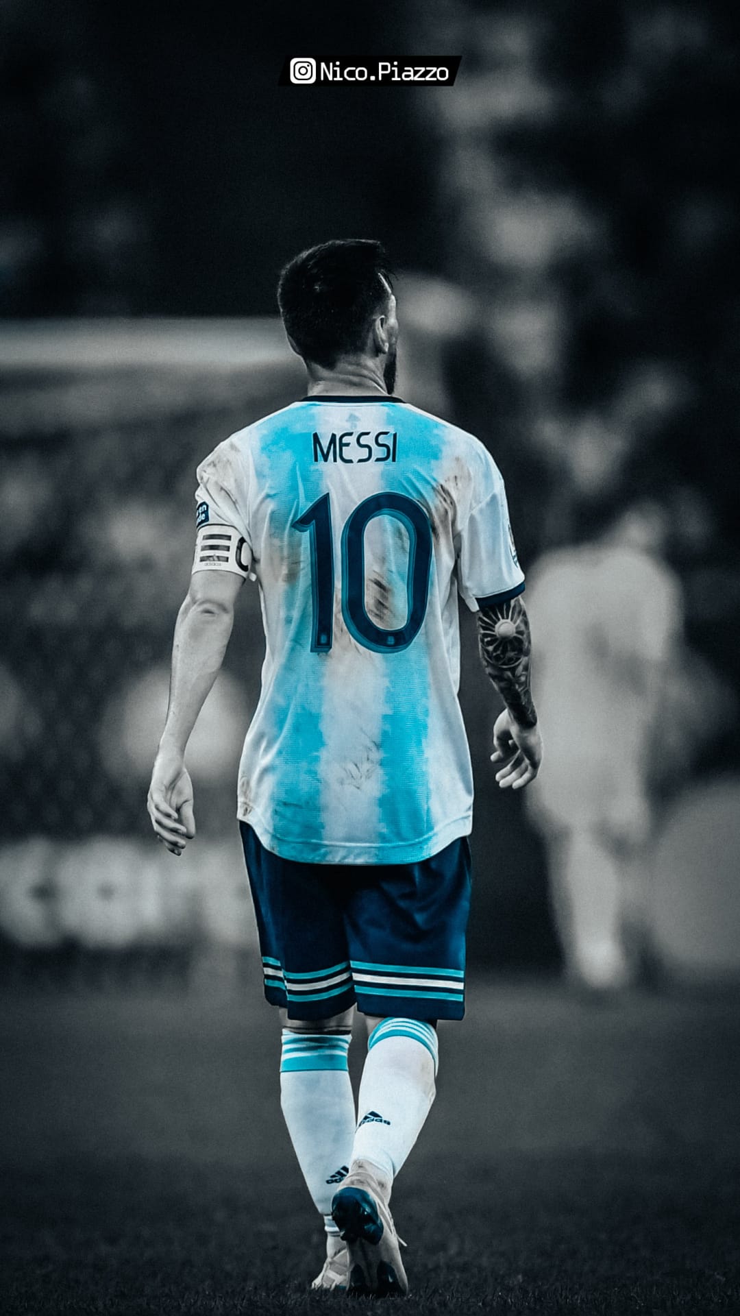 Lionel Messi seen from behind wearing an Argentina home kit with the number 10 while walking on a grass pitch.