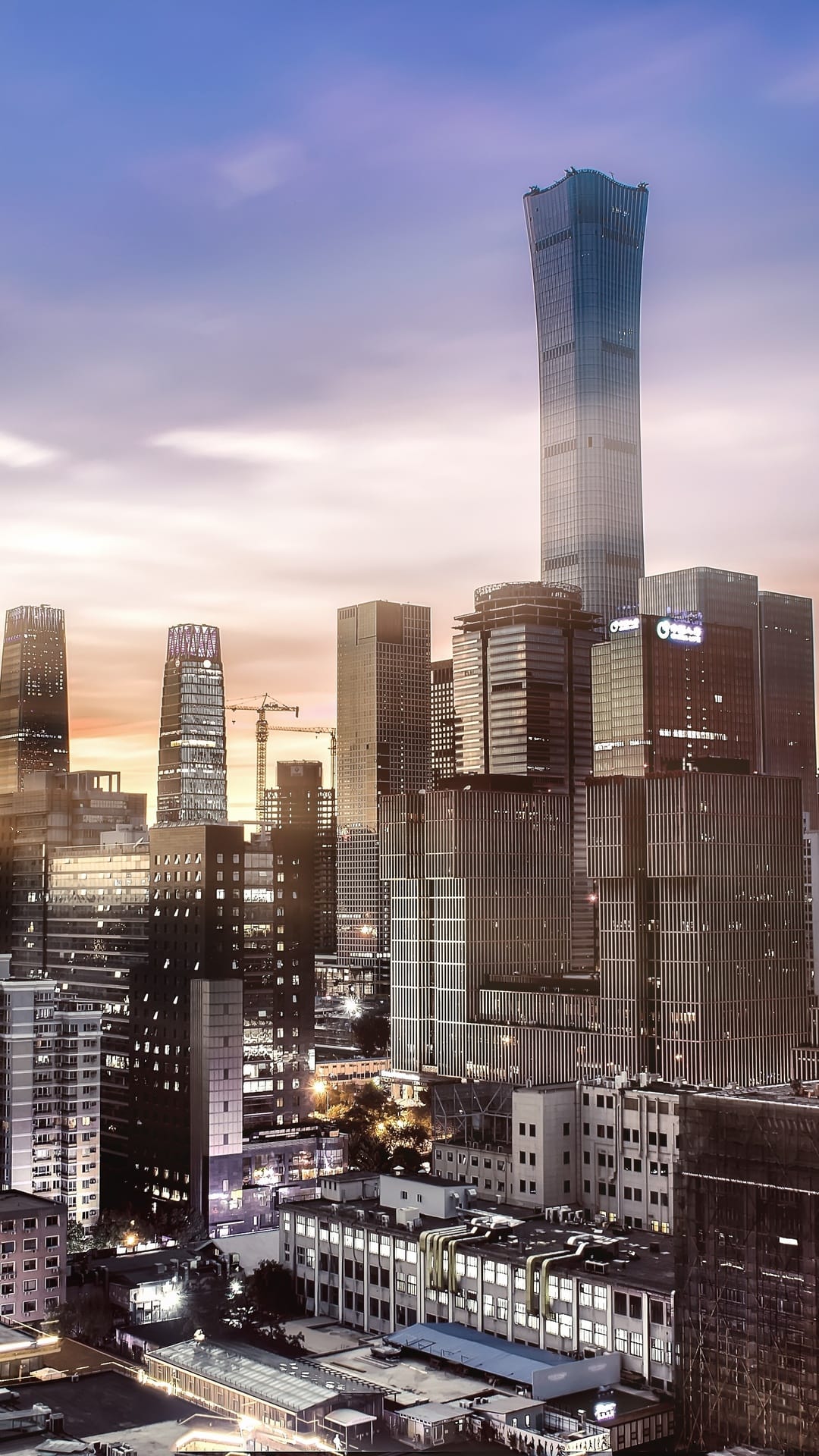 Beijing skyscrapers rise into a purple and orange gradient twilight sky with illuminated office windows.