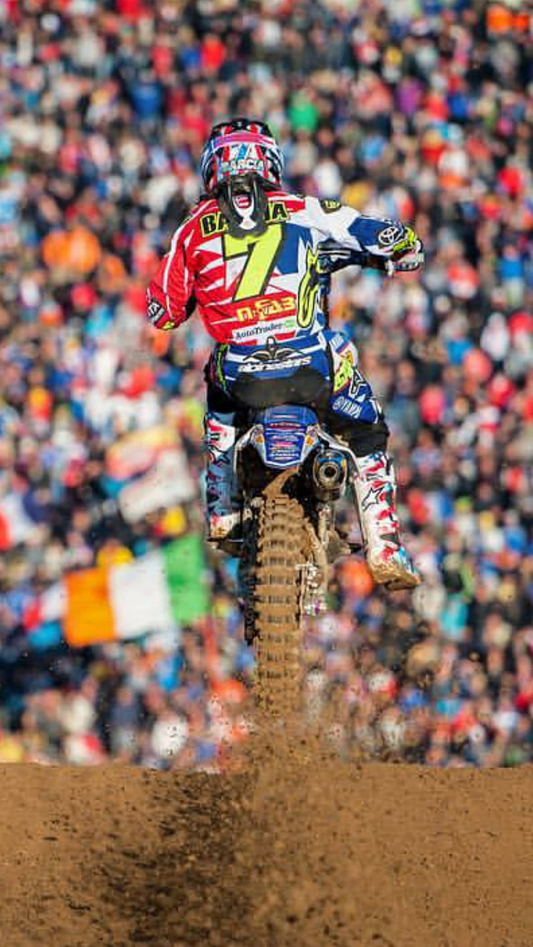 Motocross racer number seven jumps high over a stadium crowd while dirt sprays from the spinning rear wheel.