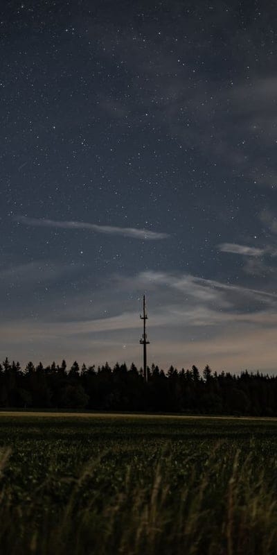 Night sky, stars, transmission tower, rural landscape, long exposure, astronomy, telecommunications, electricity, power lines, countryside, forest, trees, field, crops, nocturnal, moonlight, serene, peaceful, clear night, celestial.