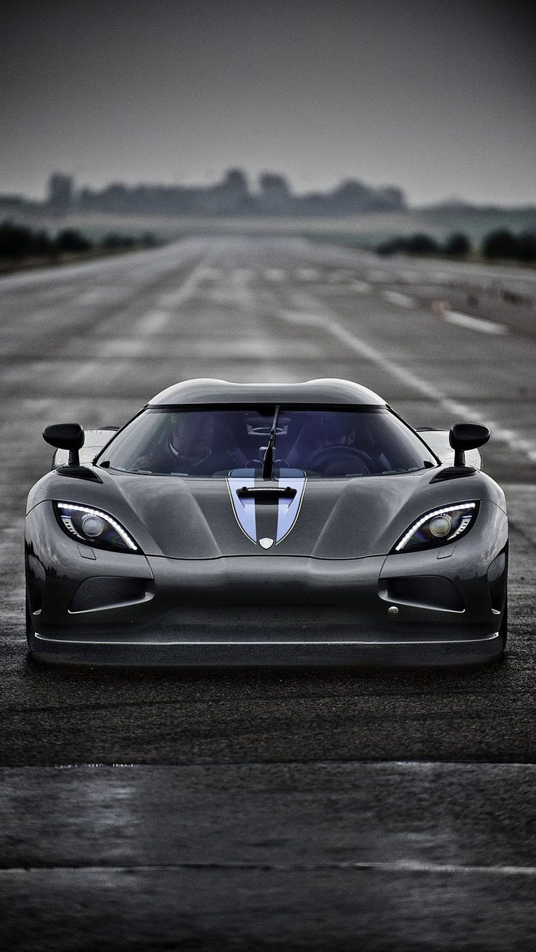 Koenigsegg Agera RS hypercar front view on wet asphalt with glowing headlights and a dark moody sky background.