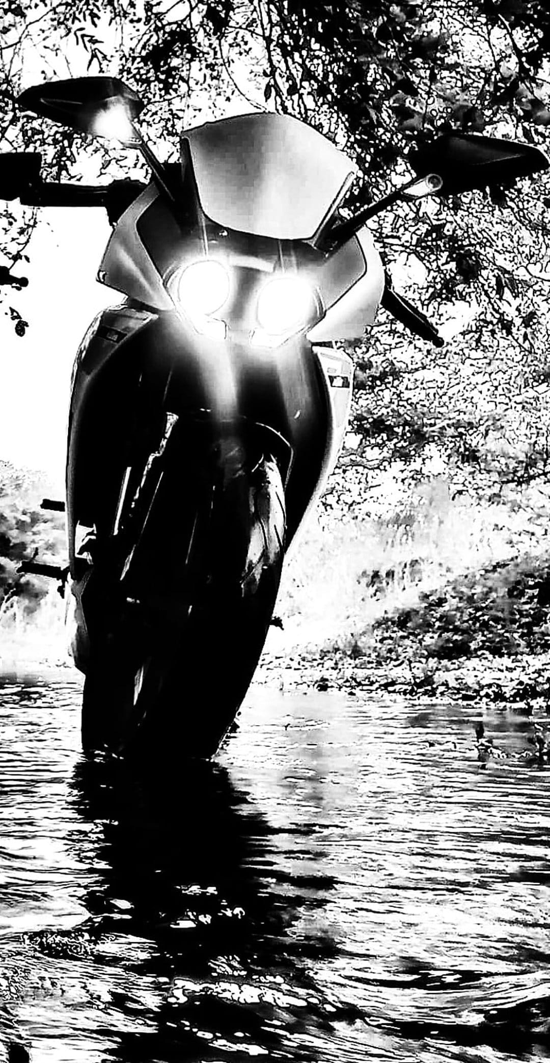 Motorcycle headlights illuminate a dark river with high-contrast reflections and surrounding dense foliage.
