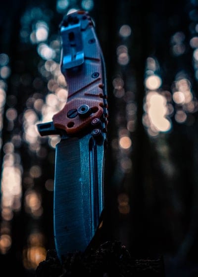 Tactical folding knife with an orange textured handle and steel blade positioned against blurred bokeh lights