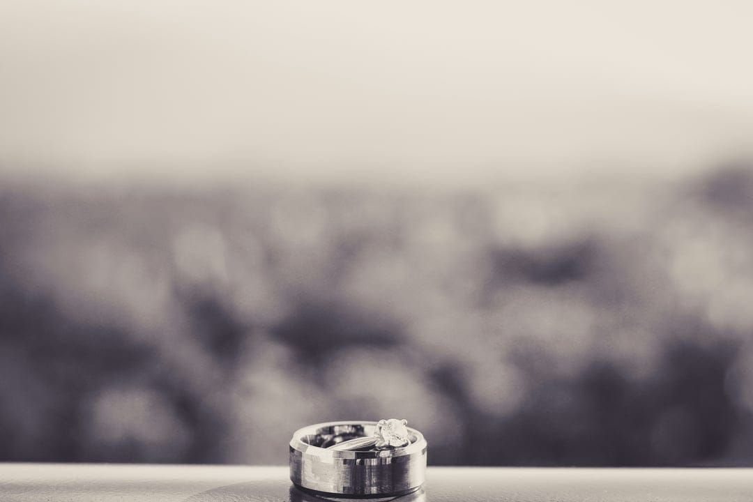 Two wedding rings with a visible diamond sparkle on a reflective surface against a soft bokeh background.