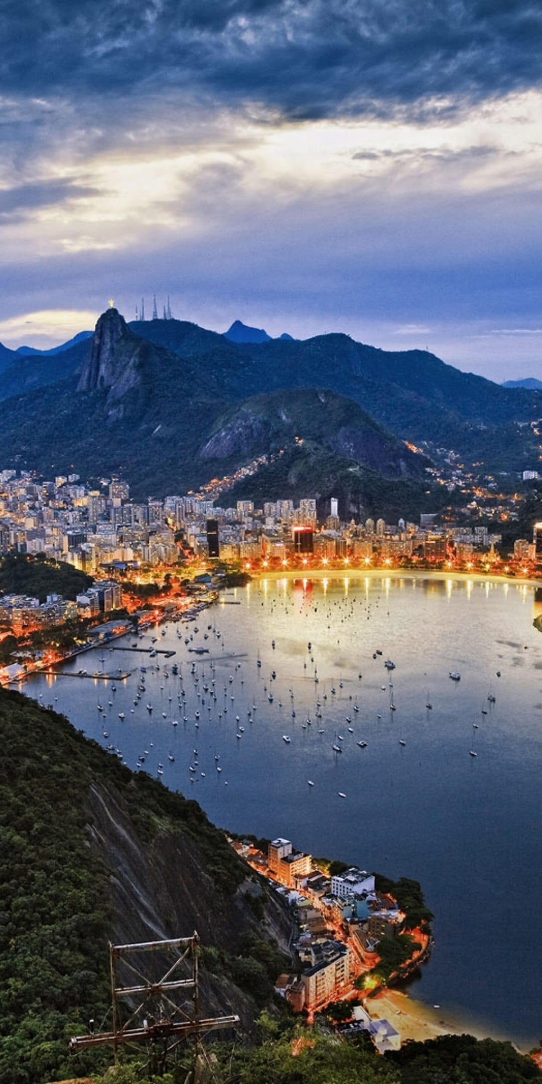 Rio de Janeiro city lights encircling Guanabara Bay at dusk with dark mountains and boats on the water.