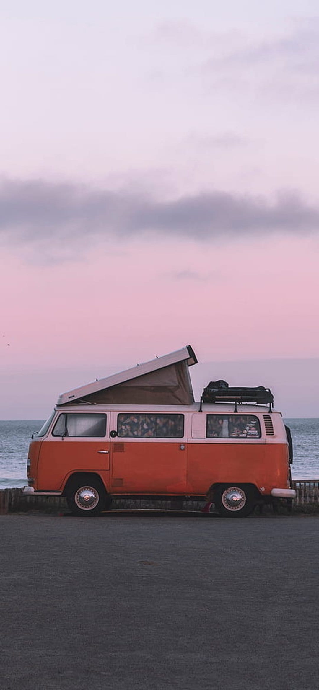 Orange and white camper van with a pop-top roof parked on a sandy beach during a pink and purple sunset.
