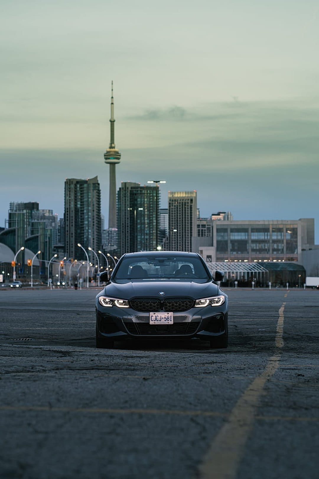 BMW sedan parked in an empty lot with the Toronto CN Tower and overcast skyline visible during a moody dusk.