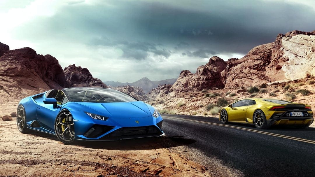 Blue and yellow Lamborghini Huracan Evo supercars on a paved road winding through rocky desert mountains.