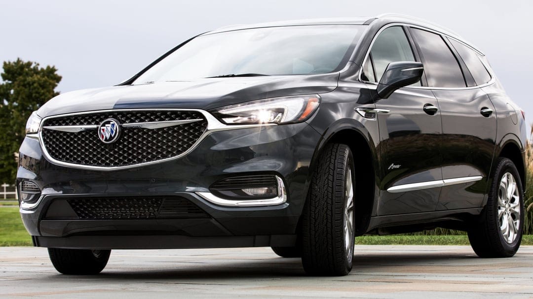 Black Buick Enclave Avenir SUV with a chrome mesh grille and glowing headlights parked on stone pavement.