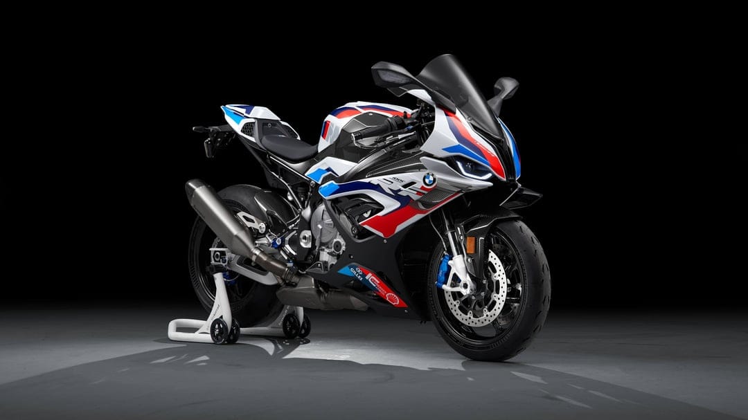 BMW M 1000 RR superbike with white, blue, and red racing livery on a paddock stand in a dark studio.