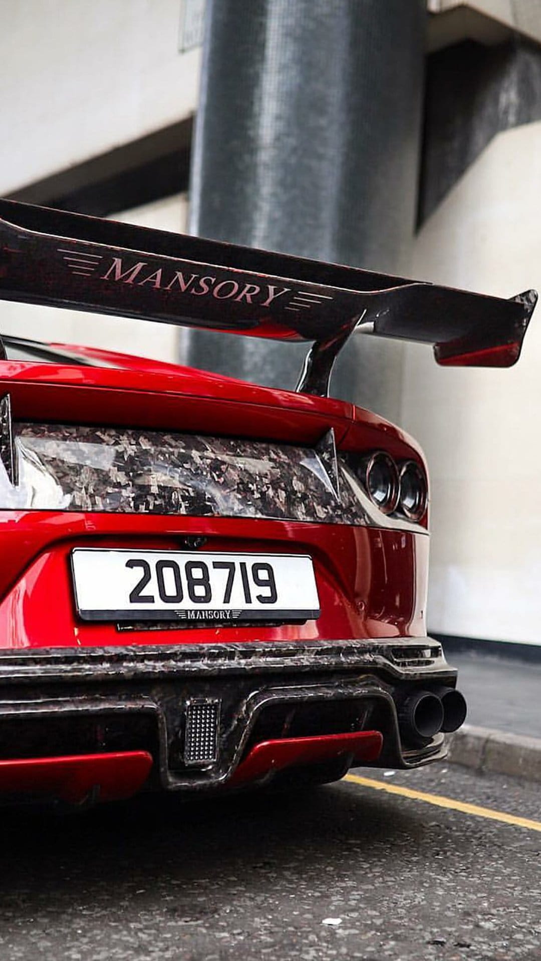 Red Mansory sports car rear wing with carbon fiber texture, dual exhausts, and a custom numeric license plate.