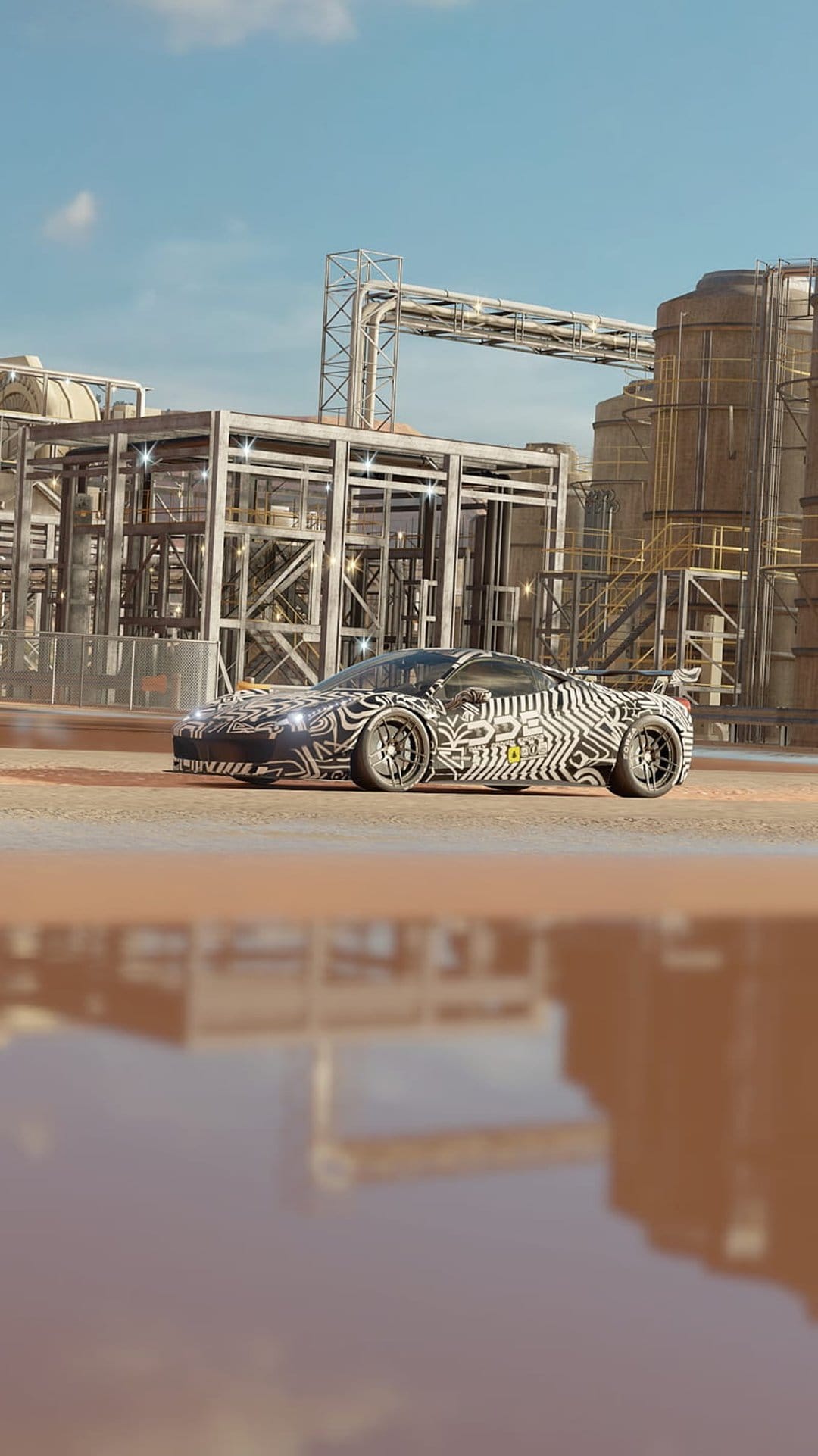 Zebra camo supercar parked near industrial pipes with a clear reflection in a foreground pool under a bright sky.