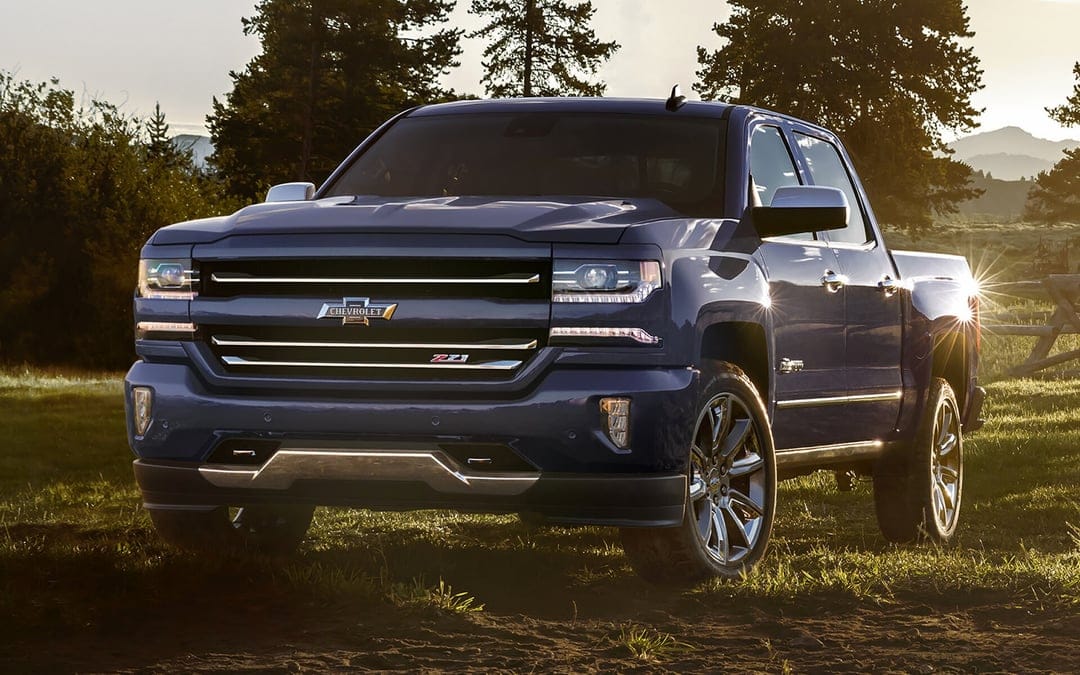 Front view of a blue Chevrolet Silverado Z71 truck in a grassy field during a golden sunset with sun glint.