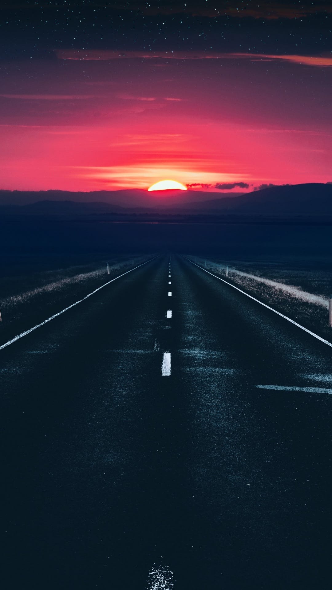 Empty asphalt road stretching toward a vibrant pink and purple sunset with faint stars in a twilight sky.
