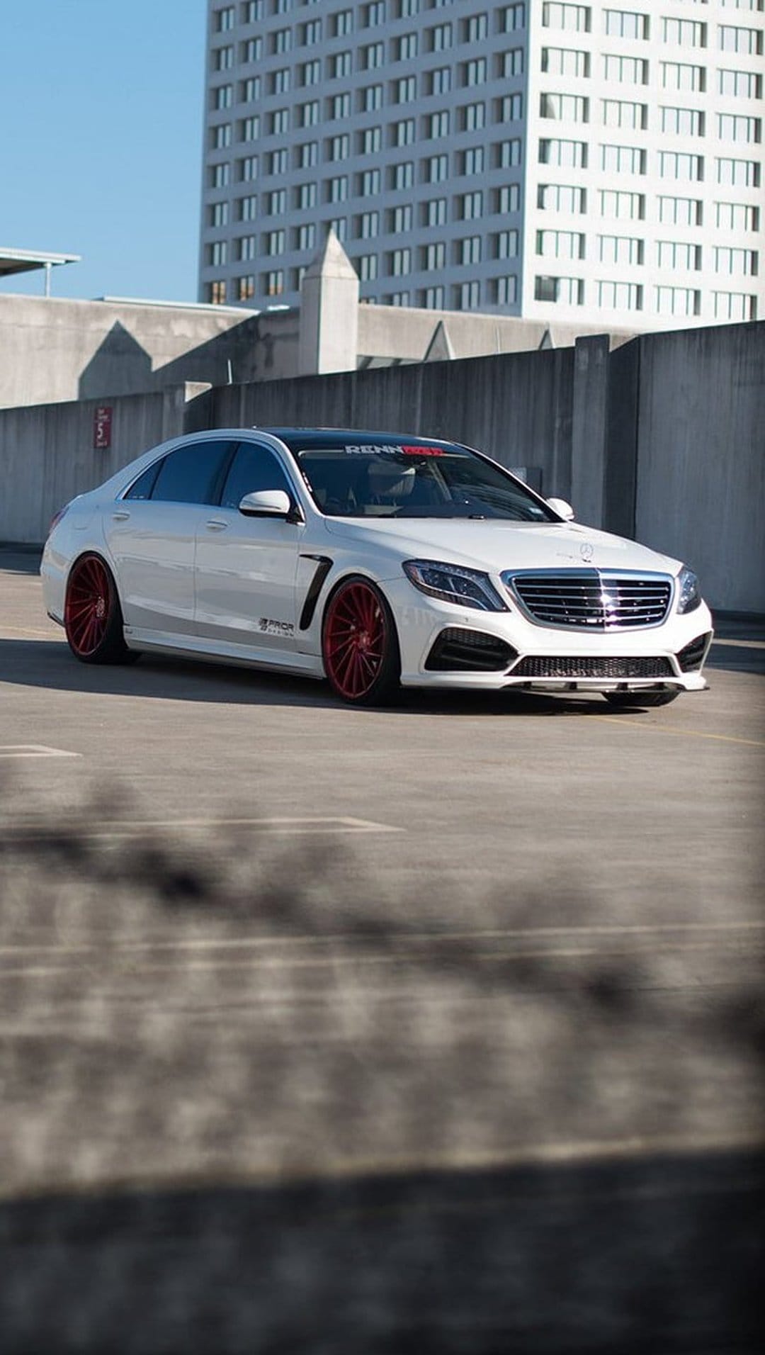 White Mercedes S-Class sedan with bright red rims parked on concrete under a clear blue sky during the day.