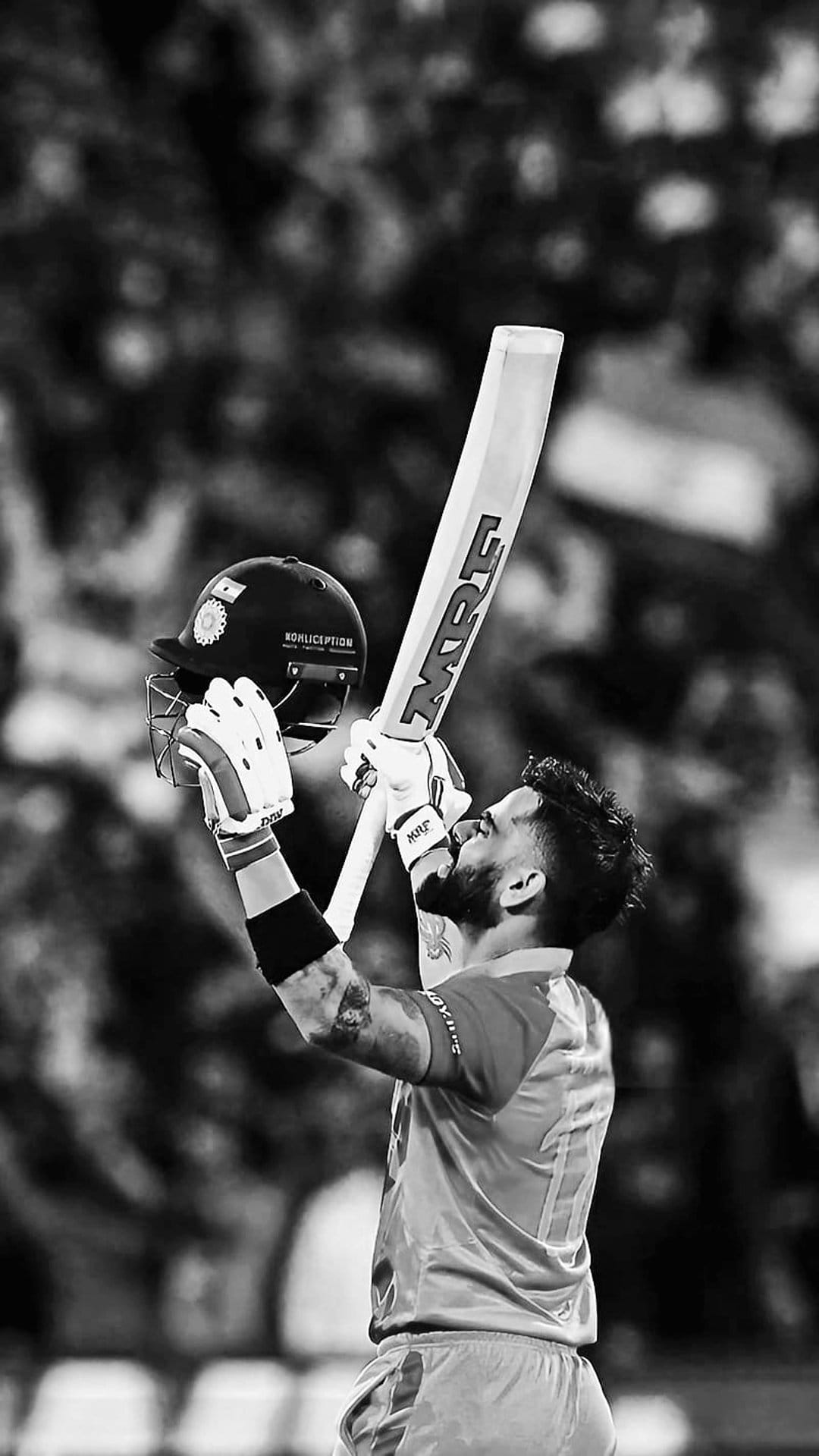 Virat Kohli kisses his cricket bat during a victory celebration in a black and white vertical sports portrait.
