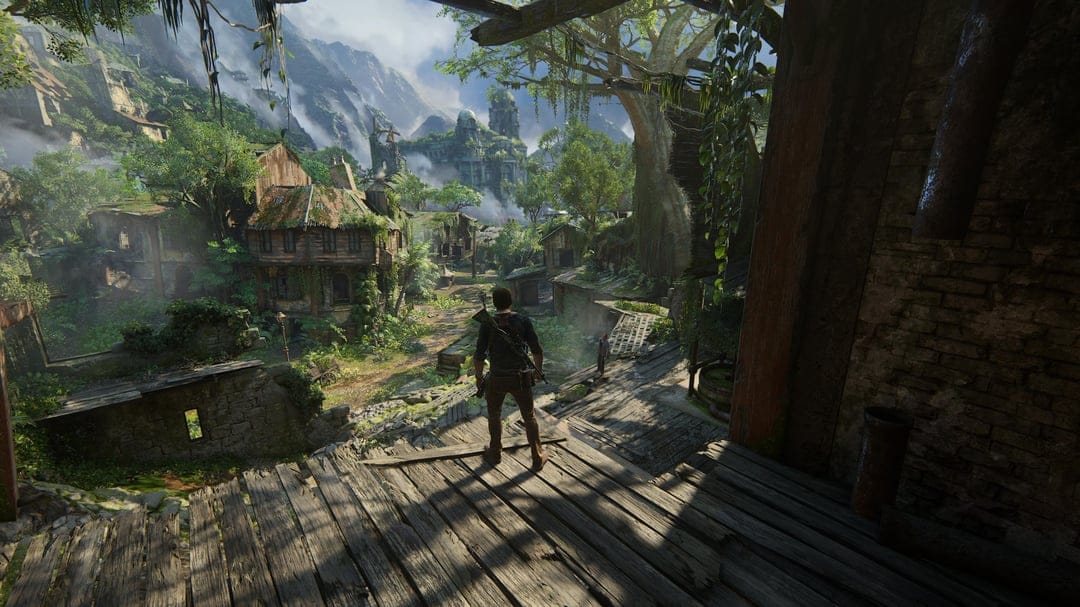 A lone traveler stands on a wooden ledge overlooking a tropical village with mountains and a waterfall.