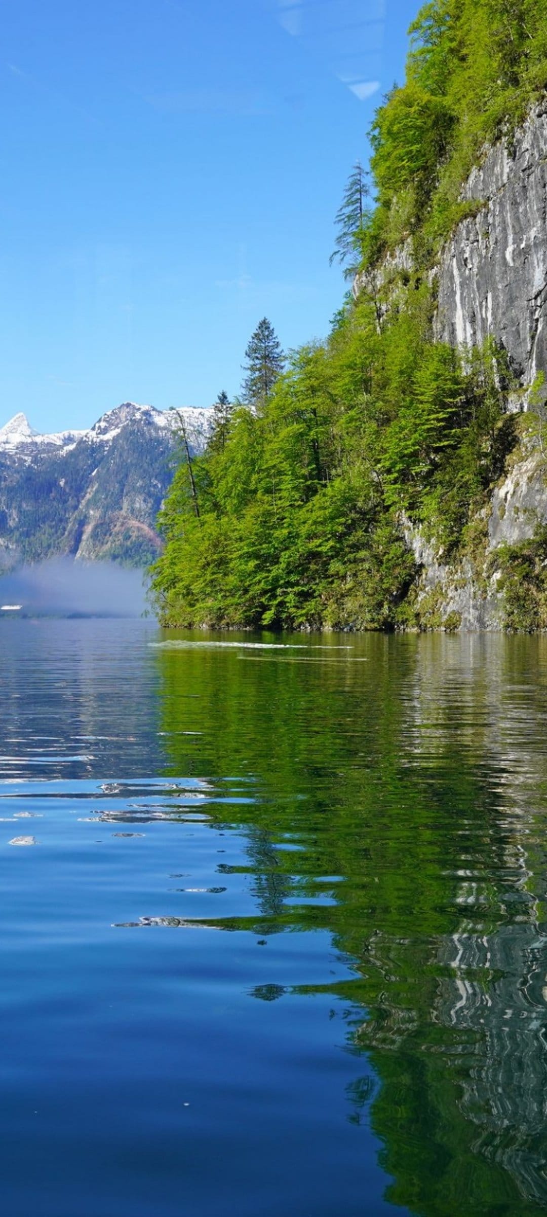 Emerald green cliffs and snow-capped peaks reflect on the calm, glassy surface of a crystal blue alpine lake.