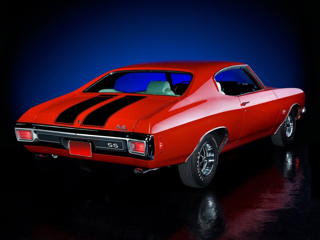 Red 1970 Chevrolet Chevelle SS with black racing stripes on a reflective black floor with blue background.