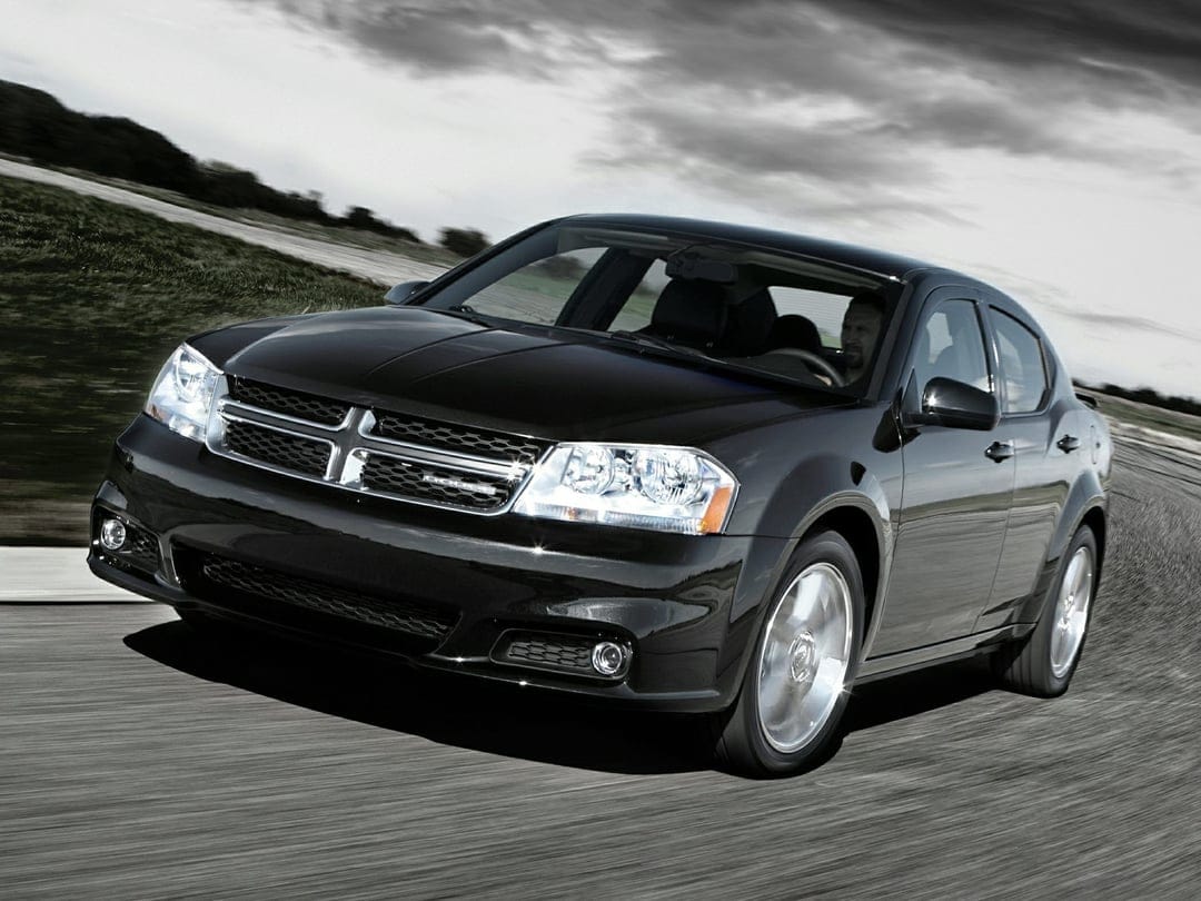 Black Dodge Avenger sedan driving fast on an asphalt road under a dramatic overcast sky with motion blur.