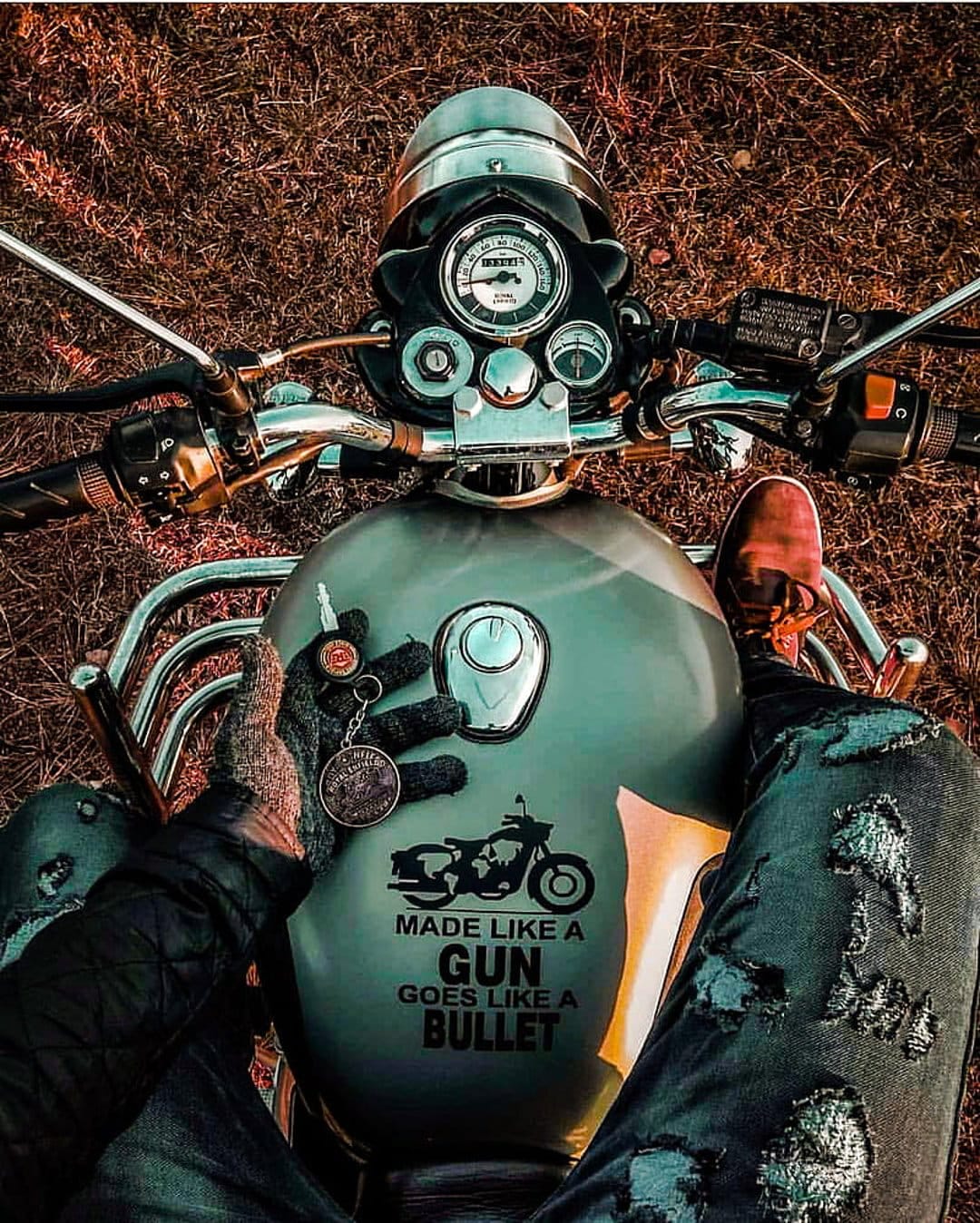 Biker sits on a vintage motorcycle showing detailed handlebars and a gloved hand holding ignition keys in dry grass.