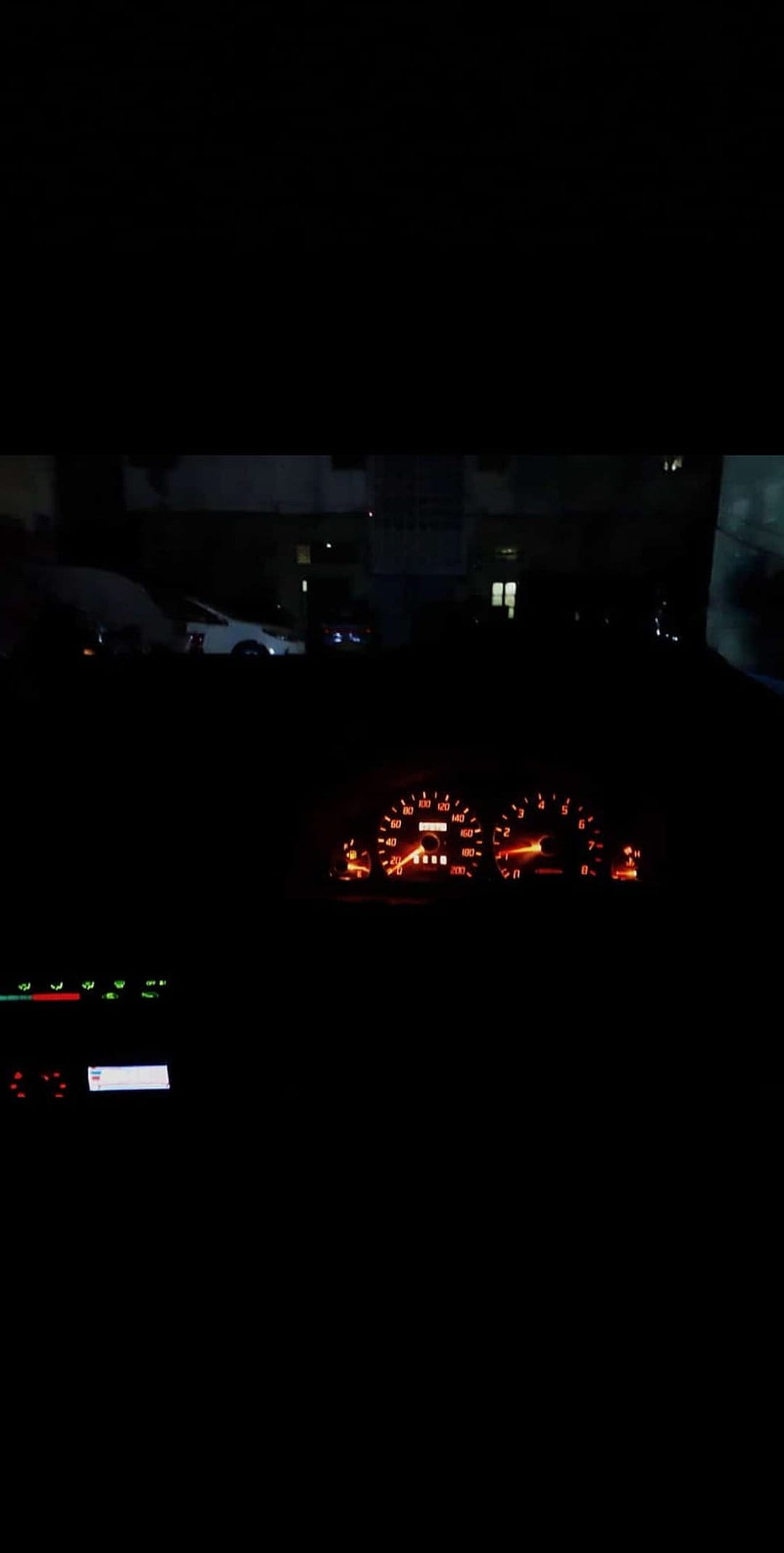 Amber-lit analog speedometer and tachometer needles glow within a dark car dashboard during a night drive.