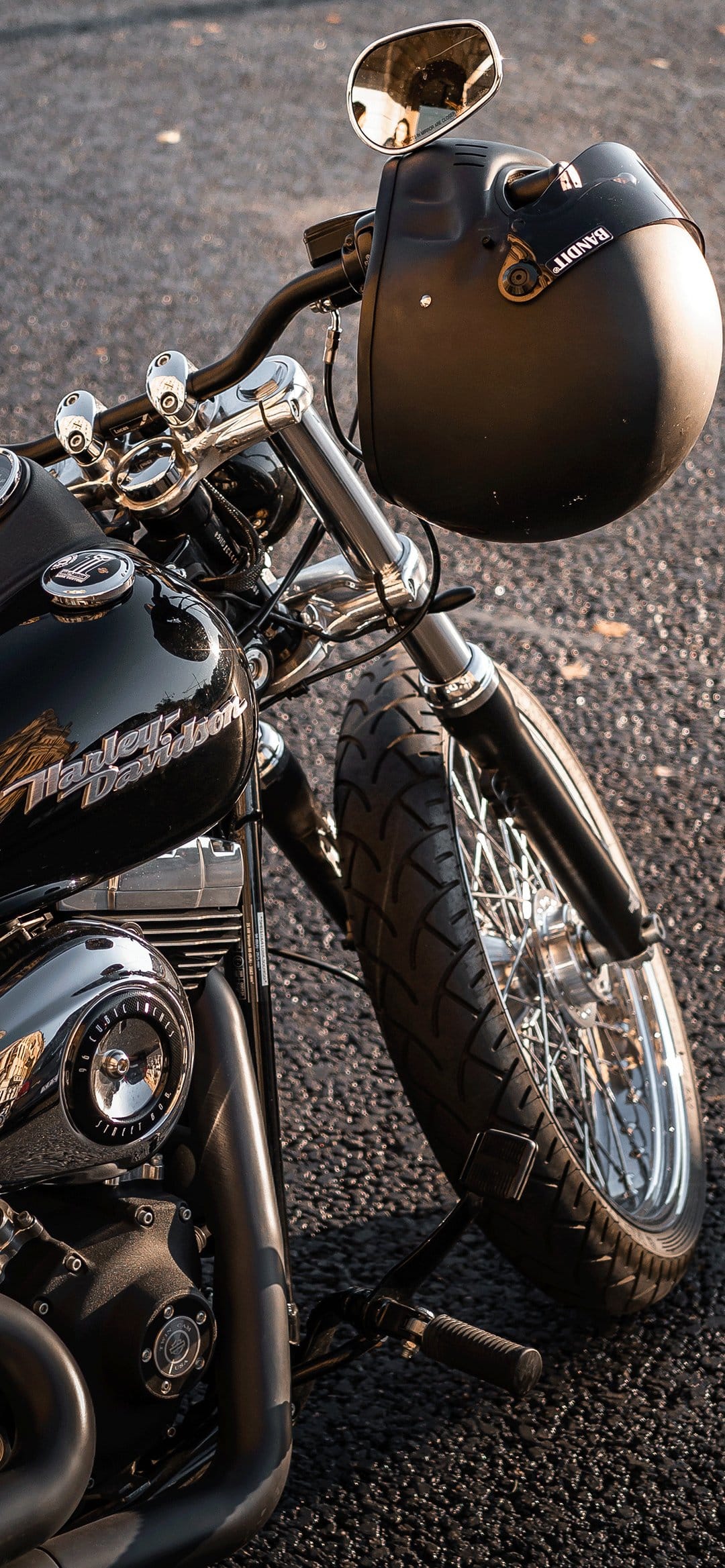 Close-up of a black Harley-Davidson motorcycle with a matte helmet on the handlebars on sunlit asphalt.