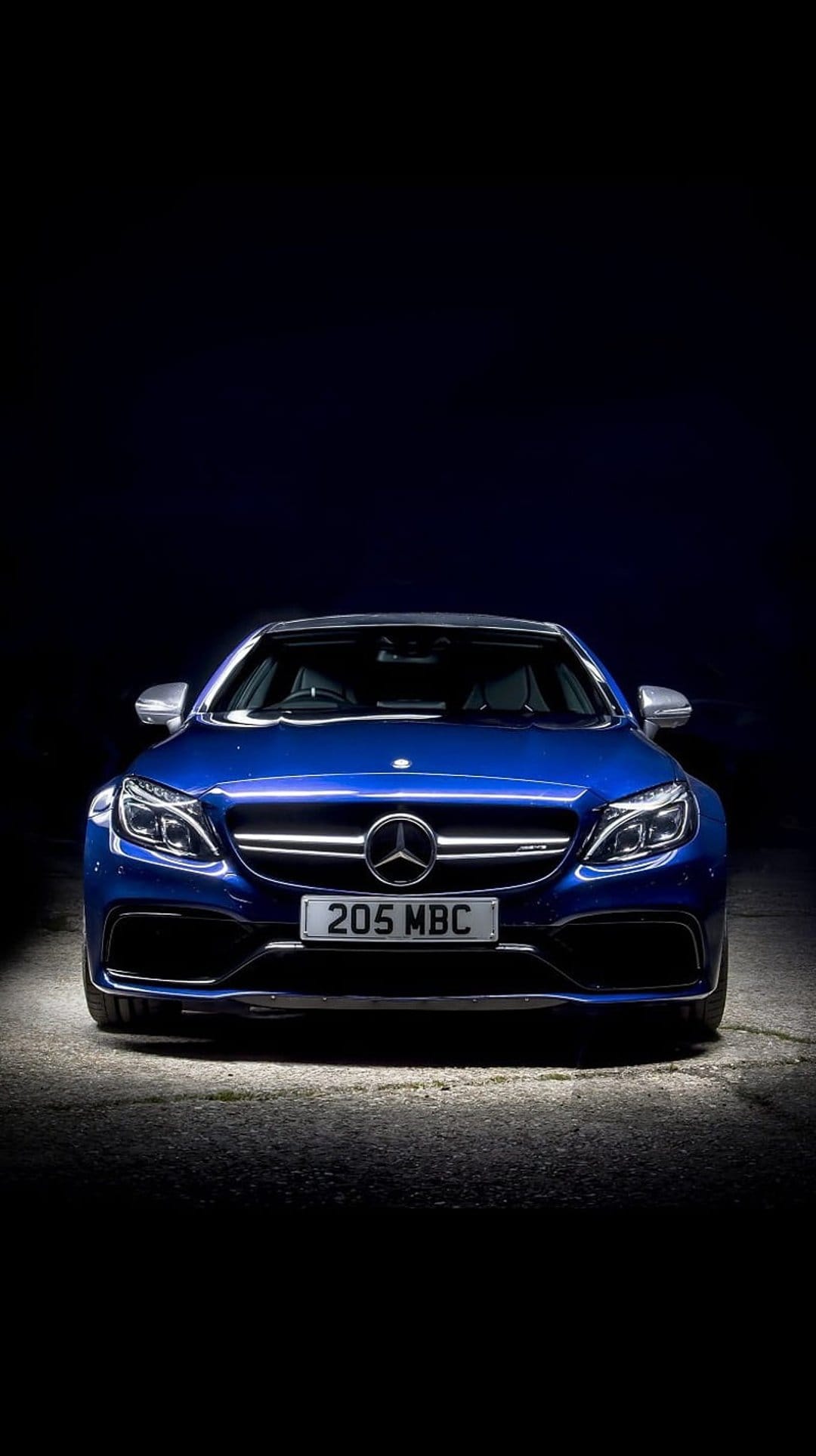 Mercedes-AMG C63 S Coupe in blue shows its front grille and headlights against a dark, dramatic background.