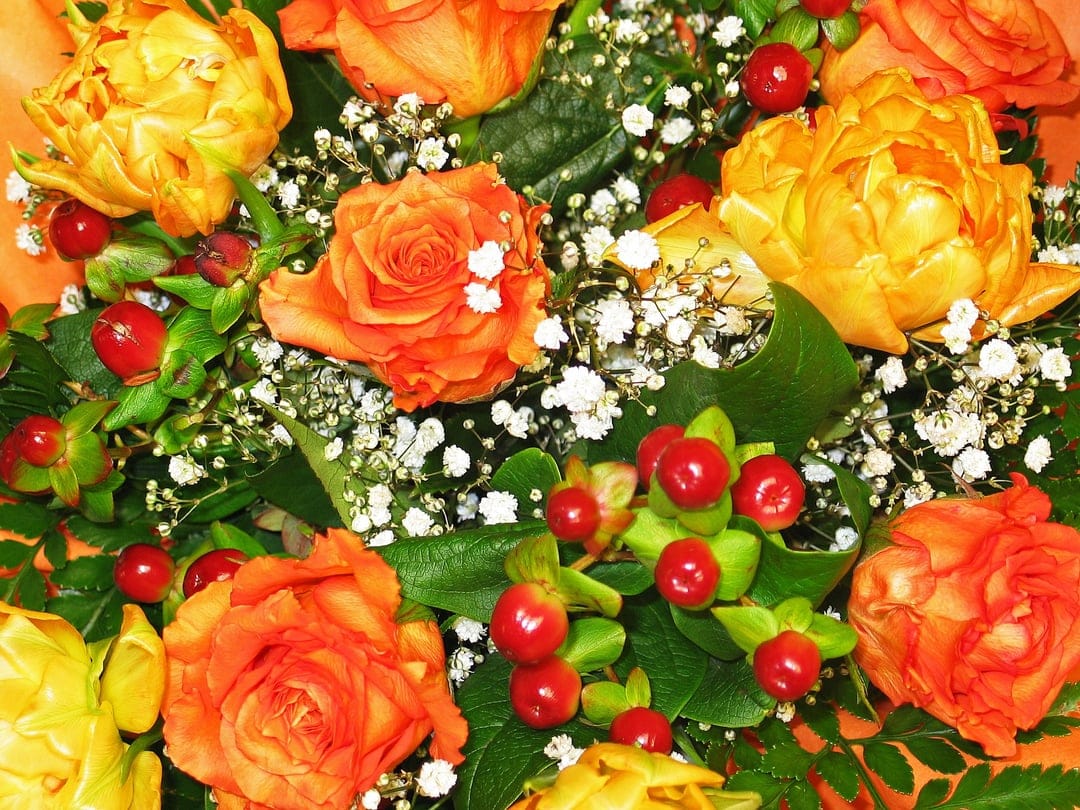 Orange and yellow roses with red berries and baby's breath petals arranged in a dense top-down floral composition.