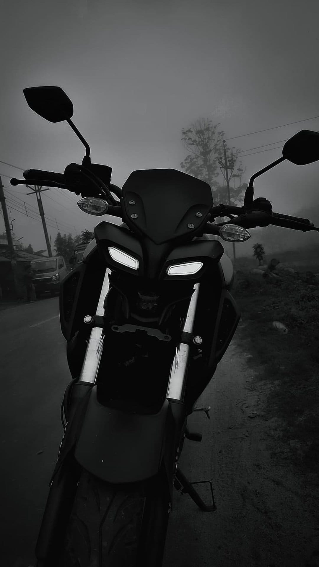 Yamaha MT motorcycle with glowing LED headlights stands on a wet asphalt road amidst thick morning fog and trees.