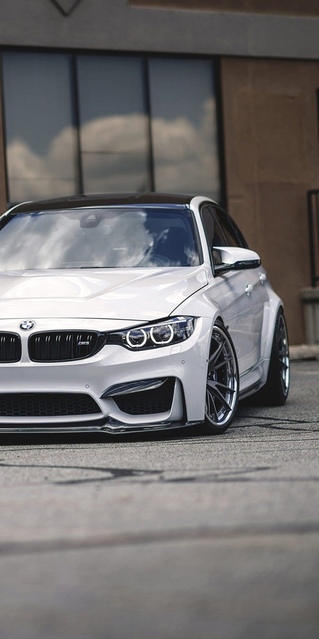 White BMW M4 coupe with flared fenders, black roof, and custom wheels viewed from a low front-angle perspective.