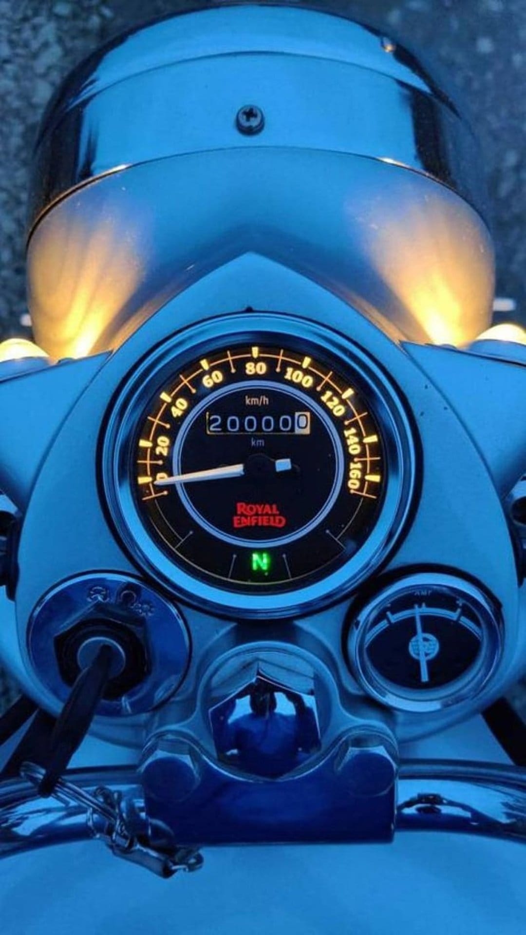 Royal Enfield speedometer glowing in low light with an odometer reading 200,000 kilometers on a chrome dashboard.