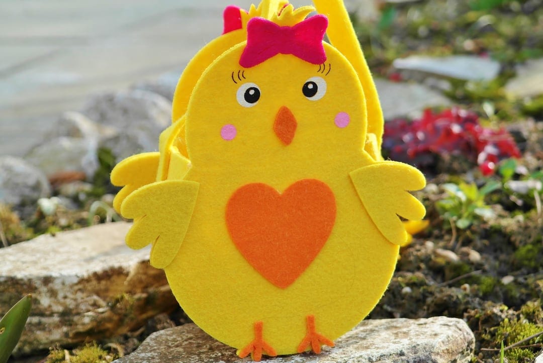 Yellow felt chick basket with a pink bow and orange heart on a soft background for an Easter egg hunt.