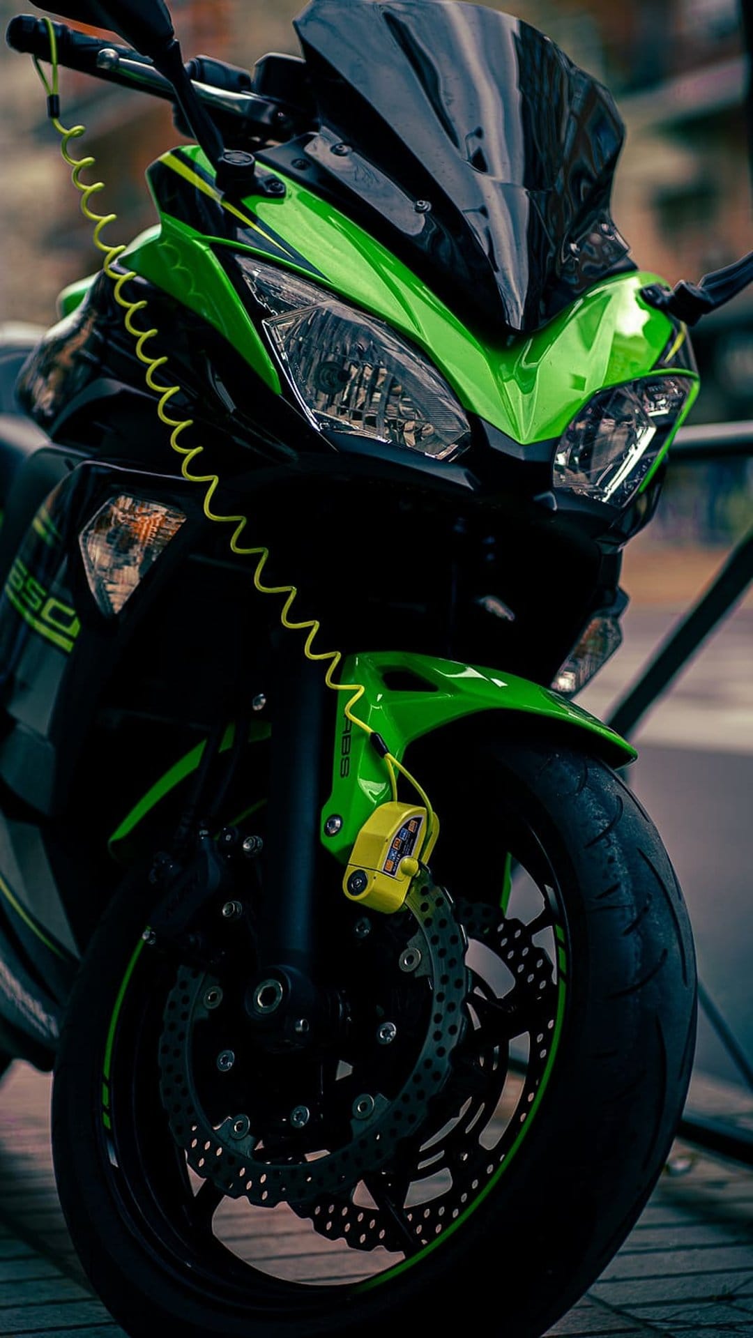Green Kawasaki motorcycle with a yellow disc lock on the front brake wheel, viewed from a low-angle perspective.