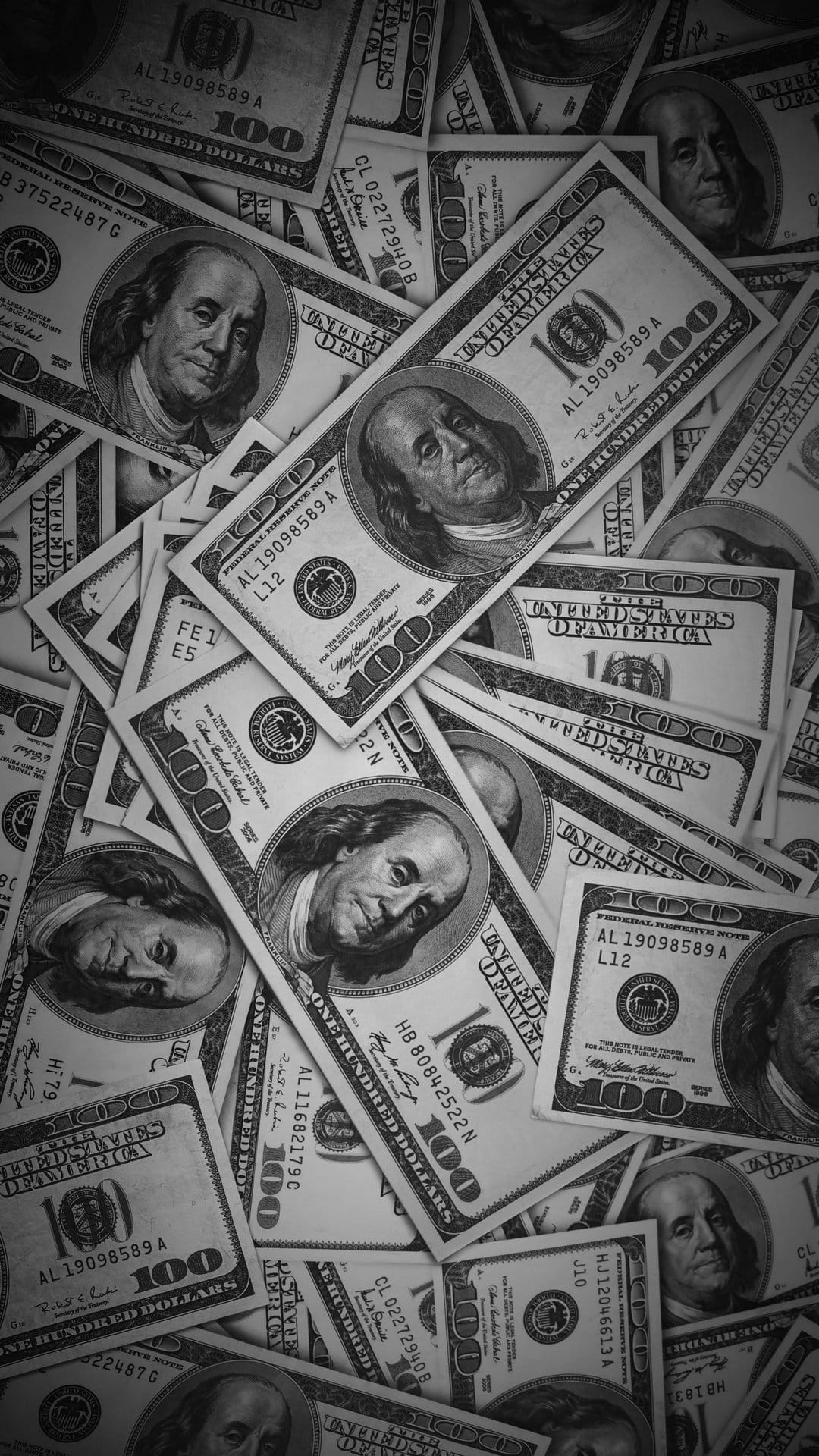 Overlapping US 100 dollar bills in a black and white overhead view featuring the portrait of Benjamin Franklin.