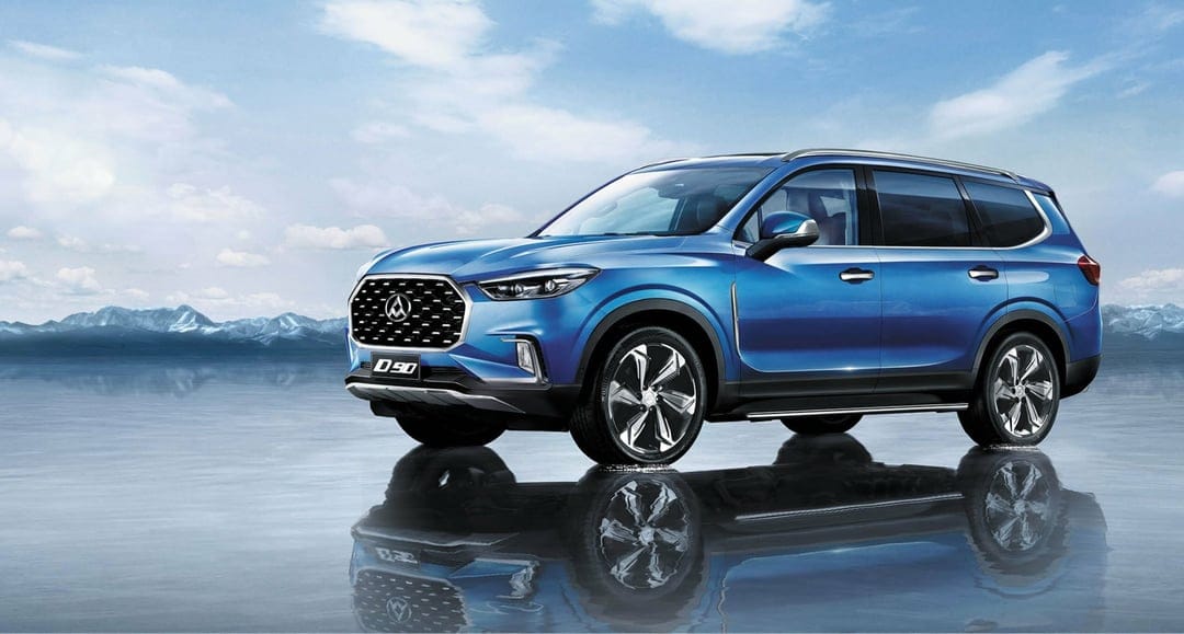 Metallic blue SUV parked on a reflective frozen lake with snow-capped mountains and cloudy blue sky behind.