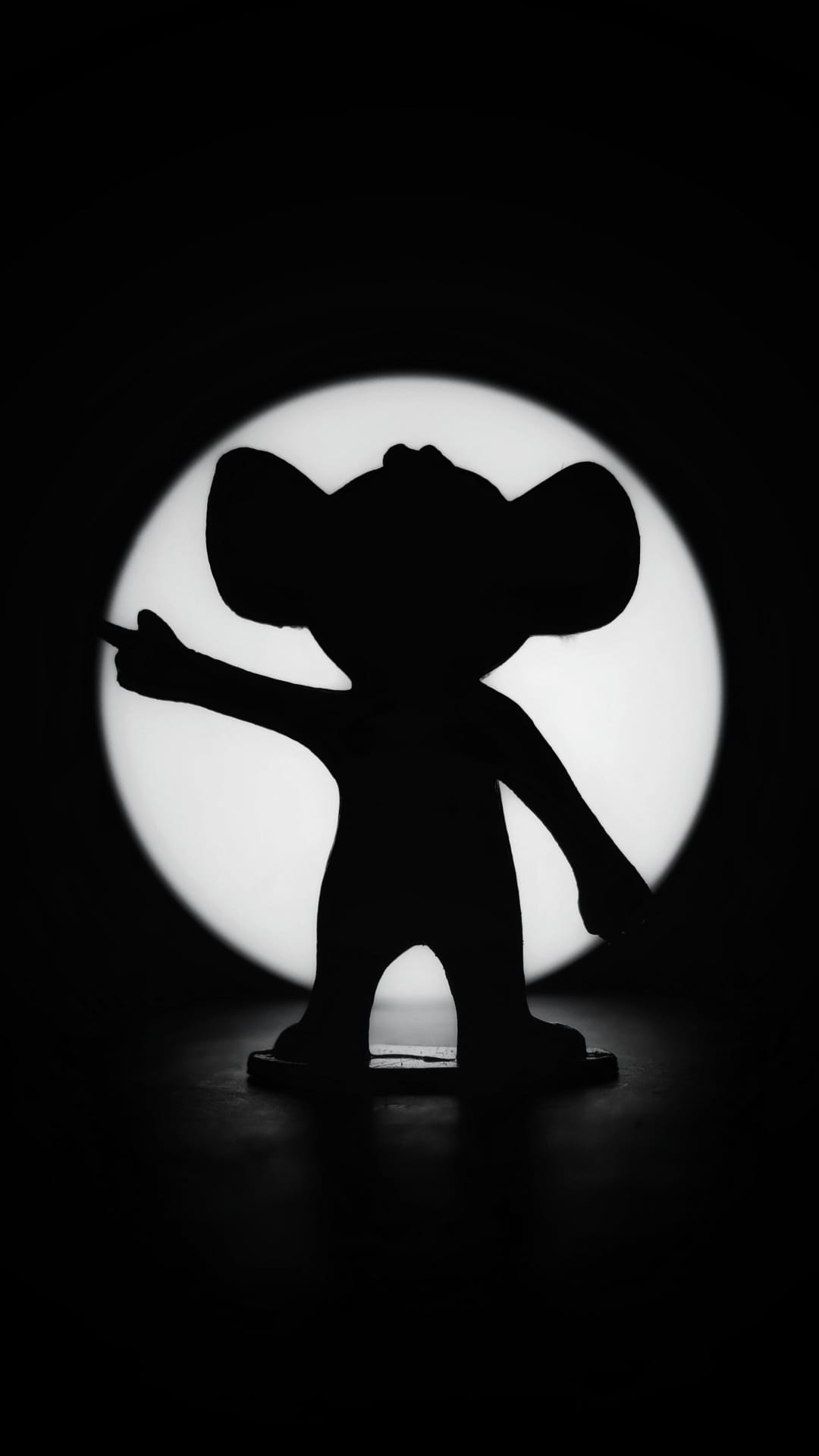 Mickey Mouse silhouette stands in profile pointing forward against a bright circular spotlight on a black background.