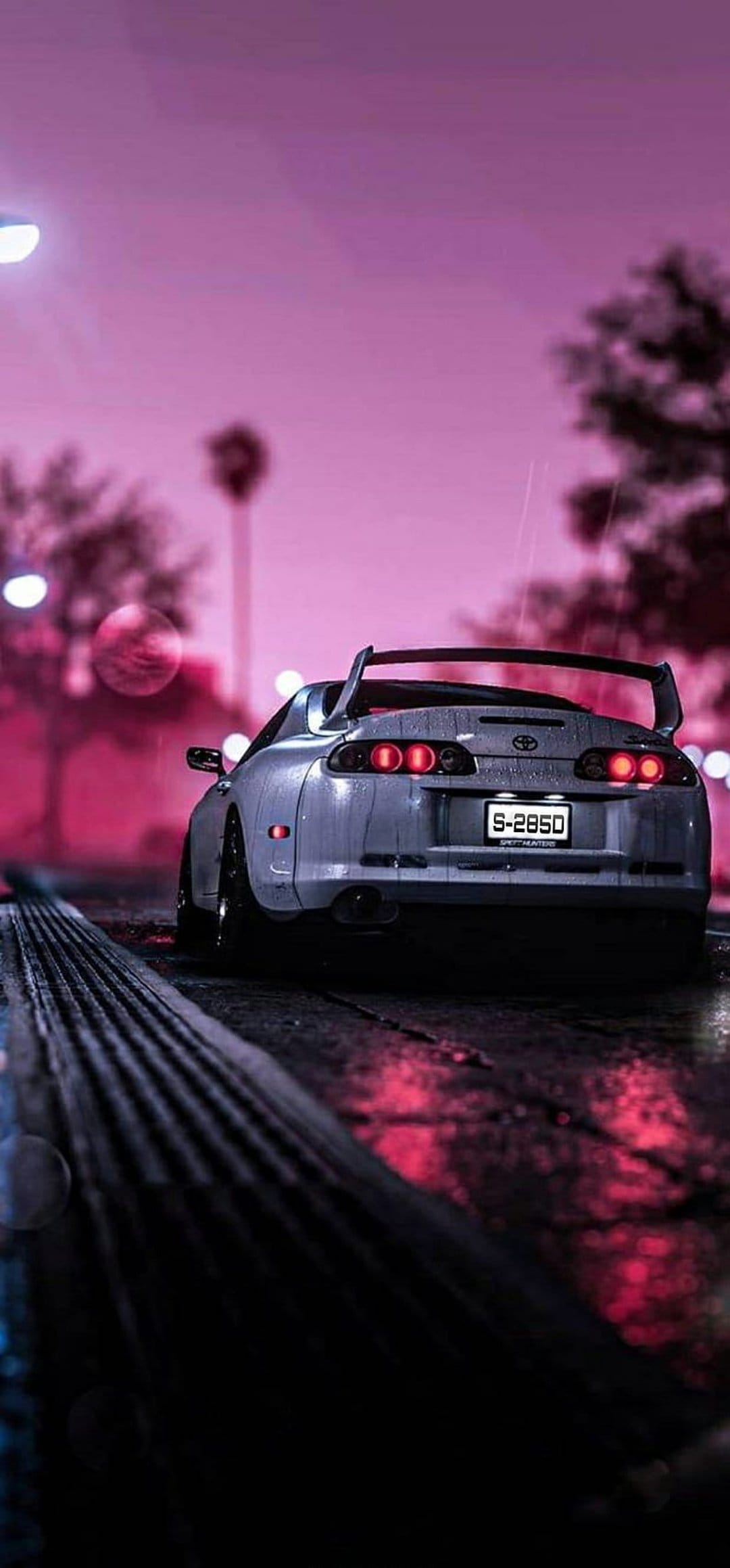 White Toyota Supra rear view on a wet night street under a pink sky with glowing red circular tail lights.
