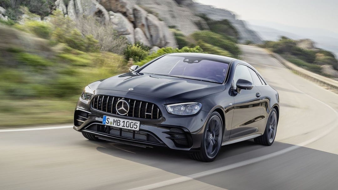 Black Mercedes-AMG E 53 Coupe driving on a curved road with rocky cliffs and motion blur in the background.