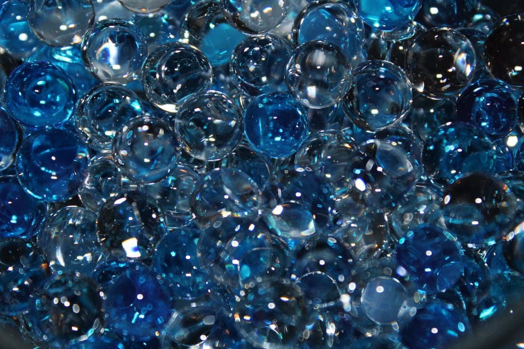 Translucent blue and clear water beads packed together with bright highlights and glossy textures in a macro view.