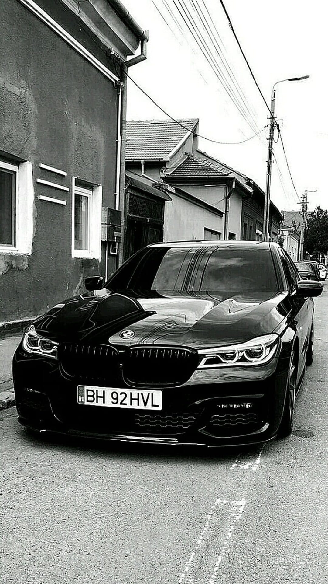 BMW sedan parked on a narrow urban street in high-contrast black and white with visible grille and headlights.