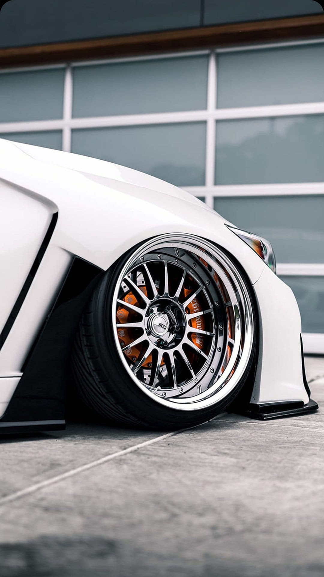 Orange brake calipers visible through a multi-spoke chrome wheel on a white sports car in a modern garage.
