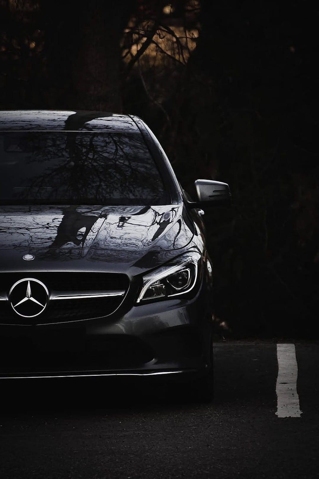 Mercedes-Benz CLA luxury sedan with glowing LED headlights and a silver star emblem on dark asphalt.