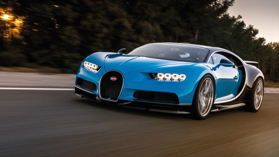 Blue Bugatti Chiron hypercar driving fast on a road with motion blur and warm sunset lighting.
