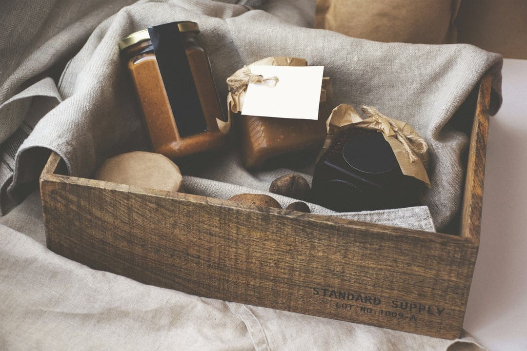 Artisanal preserve jars and whole nuts in a wooden crate lined with linen fabric for a rustic still life scene.